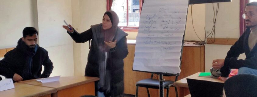 مدرّبة تشرح للمشاركين بجانب لوحة ورقية تتضمن مخططاً حول الإسعاف النفسي الأولي خلال تدريب الفريق الأول للاستجابة الميدانية