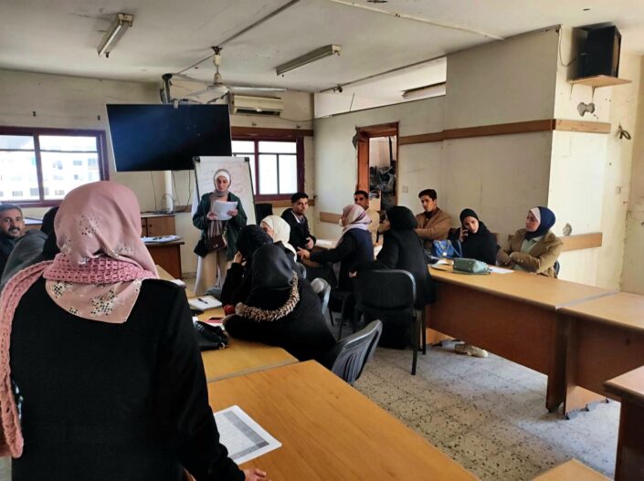 متحدثة تخاطب المشاركين الجالسين حول الطاولات في قاعة التدريب