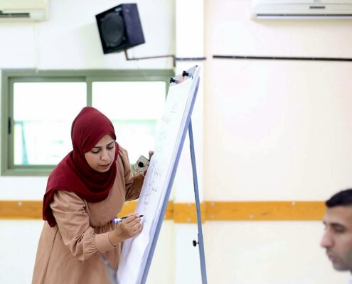 A trainer explains on a flipchart during a training session at the Center مدرّبة تكتب على اللوح الورقي خلال جلسة تدريبية في المركز الفلسطيني للديمقراطية وحل النزاعات